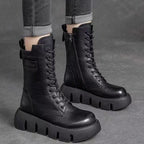 Bottes noires en cuir à semelles épaisses, style combat, portées avec un jean gris retroussé. Mode tendance, chaussures robustes, look urbain.