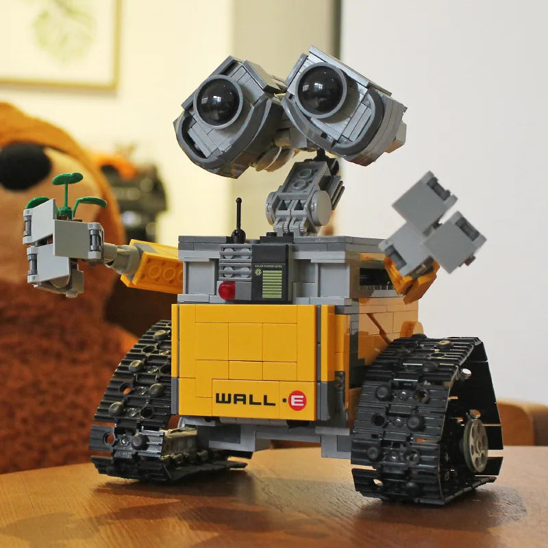 Lego Wall-E sur une table en bois, tenant une plante verte. Modèle détaillé de robot Pixar, jouet de construction populaire pour enfants et collectionneurs.