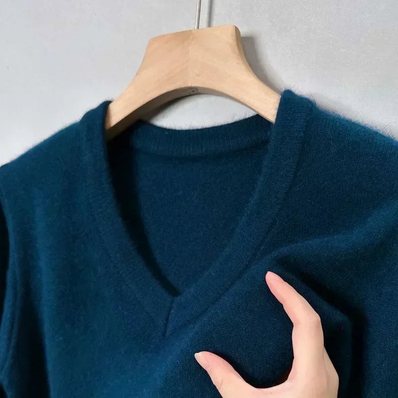Pull bleu en laine sur cintre en bois, col en V, main touchant le tissu doux. Mode hiver, vêtement chaud, style élégant et confortable.
