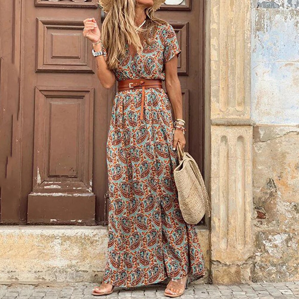 Robe longue bohème à motifs paisley, ceinturée, portée par une femme avec un sac en osier, devant une porte en bois. Mode estivale chic et décontractée.