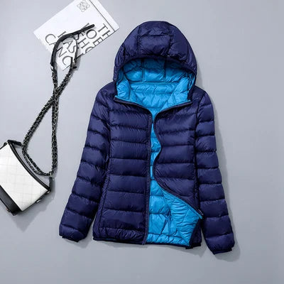 Doudoune bleue à capuche pour femme, doublure turquoise, posée à plat. Sac à main noir et blanc en arrière-plan. Mode hiver tendance.