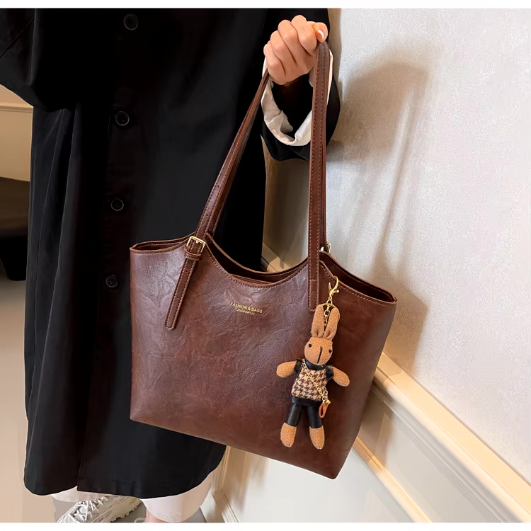 Sac à main en cuir marron avec porte-clés peluche, porté par une personne en manteau noir. Accessoire mode élégant et tendance.