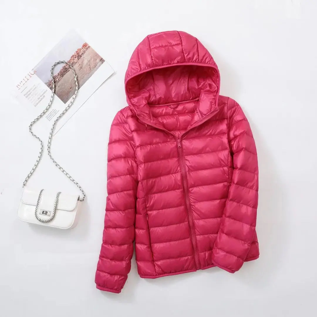 Veste doudoune rose avec capuche sur fond blanc, accompagnée d'un sac à main blanc à chaîne argentée. Mode féminine, vêtements d'hiver.