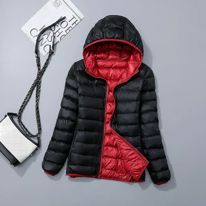 Veste doudoune noire et rouge avec capuche, posée à plat. Sac à main blanc et noir à chaîne à côté. Mode hiver, vêtements chauds.