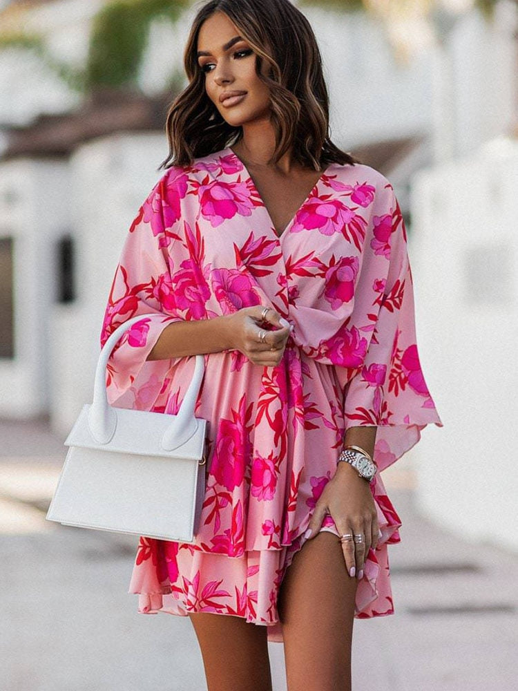 Femme portant une robe rose à motifs floraux, tenant un sac blanc. Mode estivale élégante, style décontracté chic, accessoires tendance.