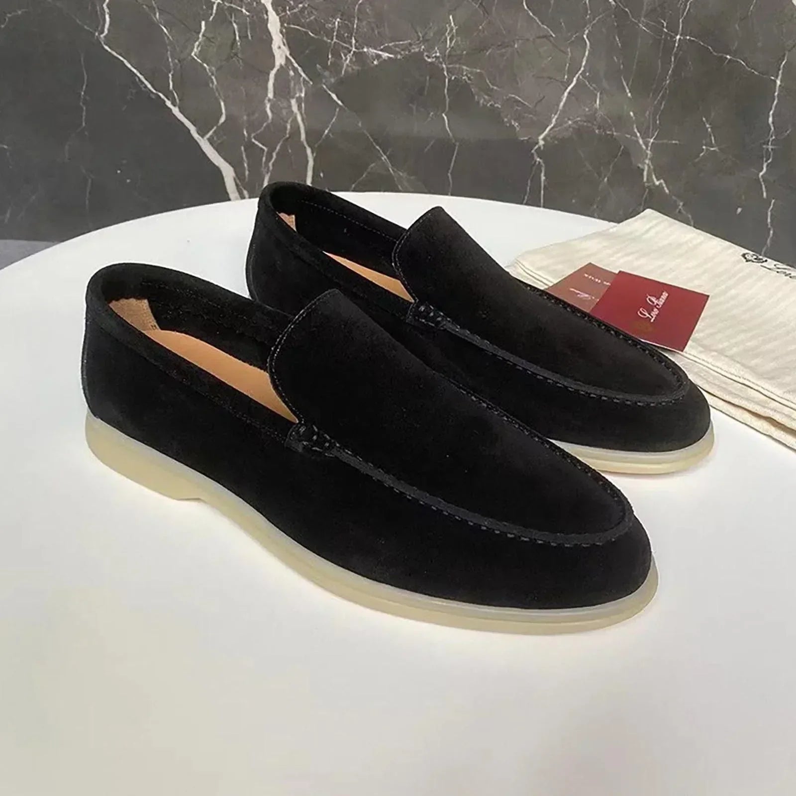 Mocassins en daim noir pour homme sur table blanche, semelle blanche, fond marbré. Chaussures élégantes, mode masculine, style décontracté.