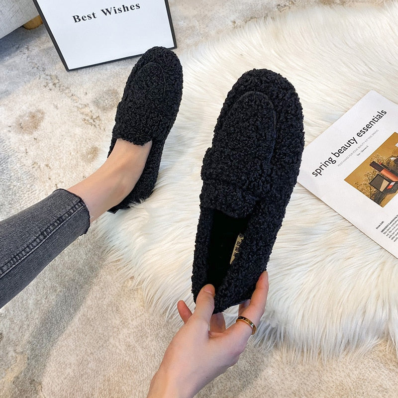 Chaussures mocassins en laine noire sur tapis blanc, tenues par une personne en jean gris. Confort et style pour l'hiver. Accessoires mode tendance.