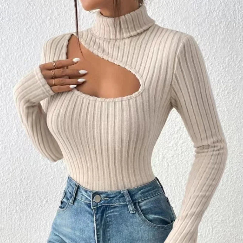 Femme portant un pull beige à col roulé avec découpe asymétrique, manches longues, associé à un jean bleu. Mode tendance automne-hiver.
