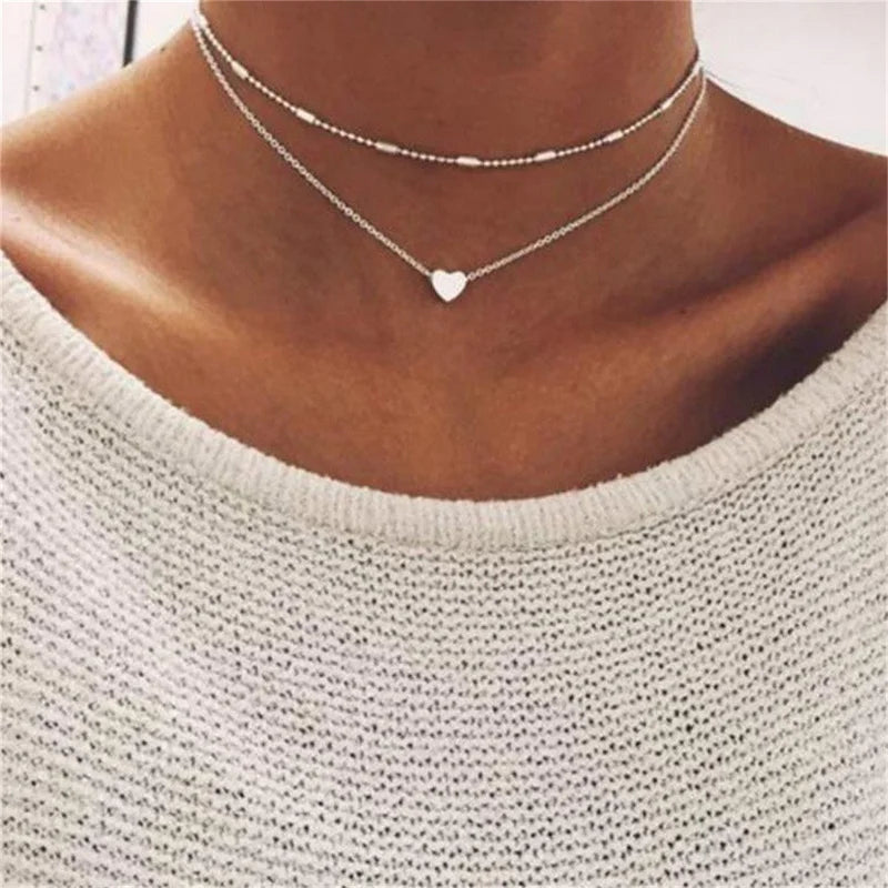 Collier double rang argenté avec pendentif cœur sur fond de pull blanc. Bijoux tendance, mode féminine, accessoire élégant.