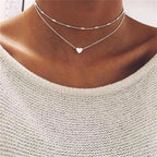 Collier double rang argenté avec pendentif cœur sur fond de pull blanc. Bijoux tendance, mode féminine, accessoire élégant.