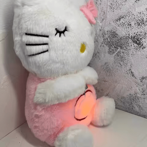 Peluche Hello Kitty rose et blanche, assise contre un mur texturé, avec un nœud rose et un ventre lumineux. Jouet enfant populaire et mignon.