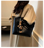 Femme portant un sac à main noir en cuir avec un porte-clés lapin, manteau beige, intérieur moderne. Accessoire mode tendance, élégant.