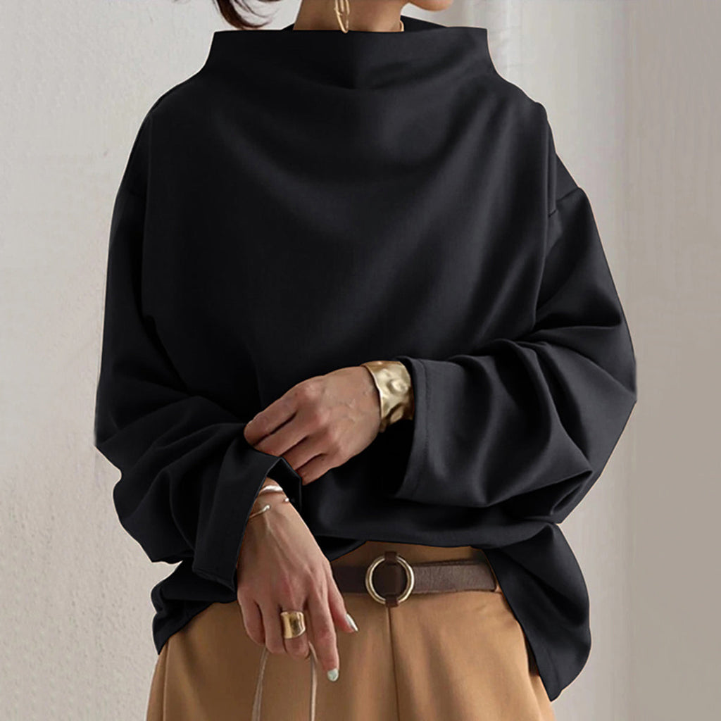 Femme portant un pull noir ample à col montant, manches longues, avec pantalon beige et ceinture marron. Mode automne-hiver élégante et décontractée.