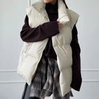 Veste sans manches matelassée beige sur pull noir, jupe à carreaux. Mode automne-hiver, tenue décontractée, style moderne et tendance.