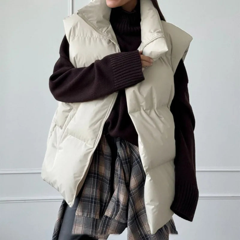 Veste sans manches matelassée beige sur pull noir, jupe à carreaux. Mode automne-hiver, tenue décontractée, style moderne et tendance.