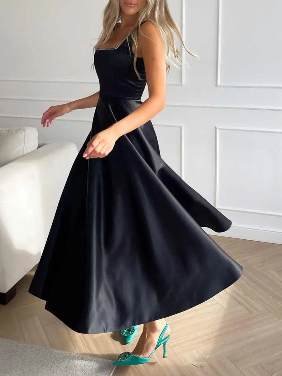 Femme en robe noire élégante tournoyante, chaussures vertes, intérieur moderne, parquet clair, mur blanc. Mode chic, style soirée, glamour.