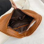 Sac à main en cuir tressé marron ouvert, intérieur doublé avec poche zippée, main tenant le sac. Accessoire mode élégant et tendance.