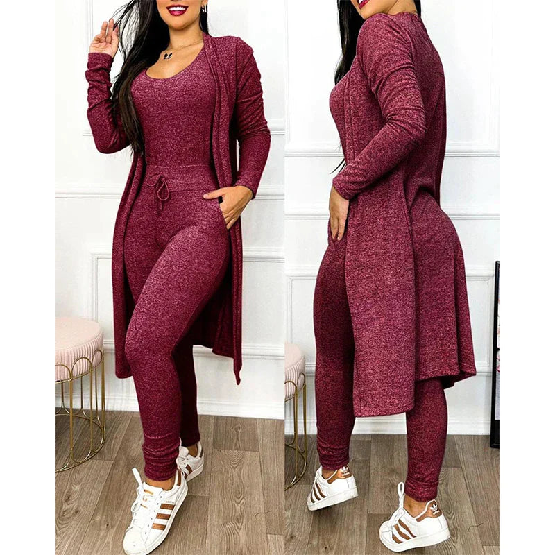 Femme portant un ensemble bordeaux en tricot, composé d'un long cardigan, d'un débardeur et d'un pantalon ajusté, avec des baskets blanches.