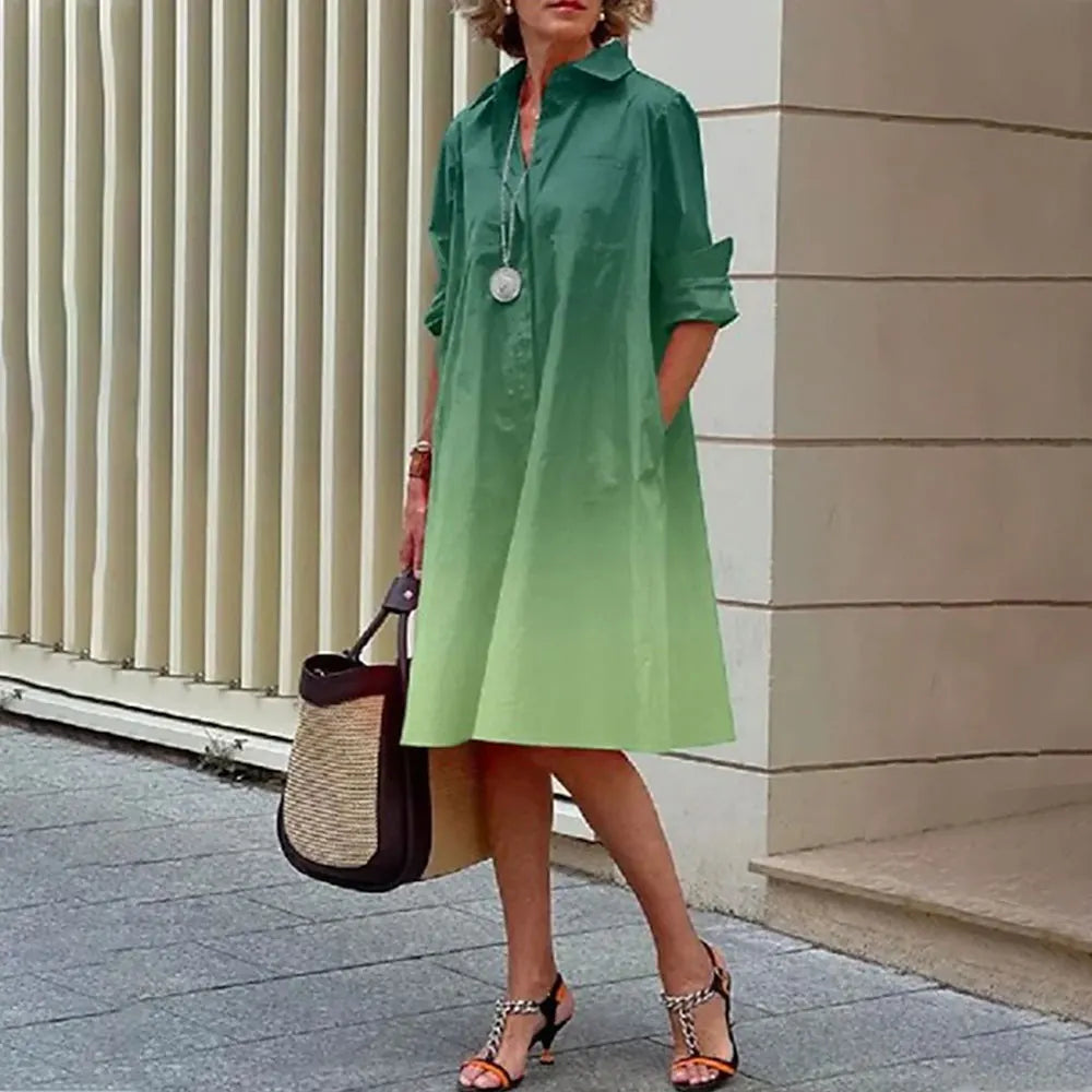 Robe chemise verte dégradée, manches retroussées, portée par une femme avec sac en paille et sandales à talons, devant un mur moderne.