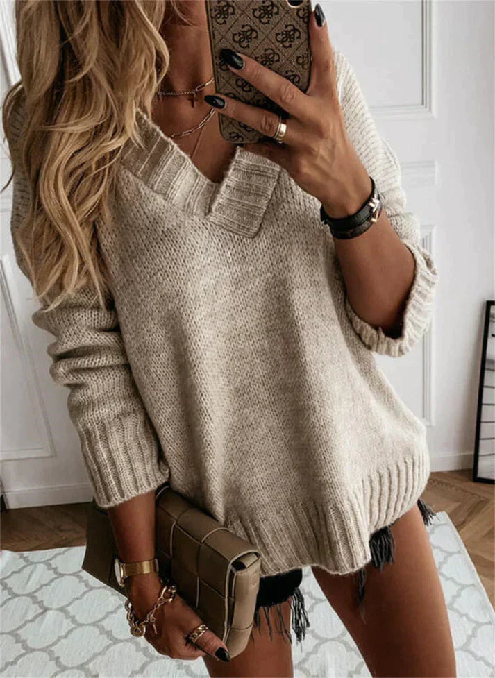 Femme portant un pull en tricot beige, manches longues, avec un sac à main marron. Style décontracté chic, cheveux blonds ondulés.