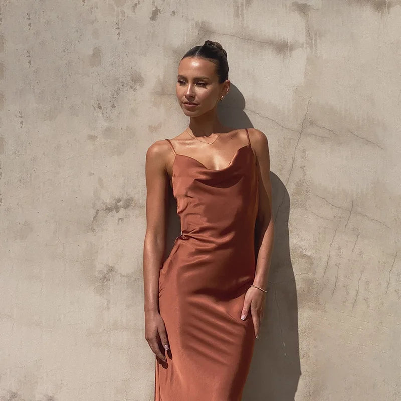 Dame en robe satinée orange posant contre un mur texturé. Mode élégante, tenue chic, style minimaliste, robe soirée tendance.