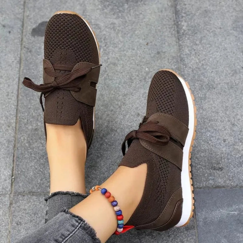 Chaussures de sport marron pour femme, en maille respirante, avec lacets et semelle blanche, portées avec un jean gris et bracelet coloré.