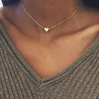 Collier ras du cou en or avec pendentif cœur sur fond de pull gris texturé. Bijoux élégants, mode féminine, accessoire tendance.