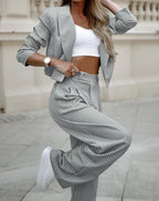 Femme en tailleur gris à rayures, top blanc, montre élégante, pose décontractée. Mode féminine chic, tendance urbaine, style moderne.