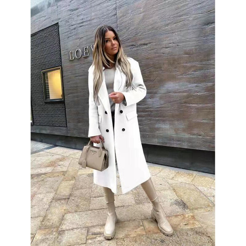 Femme portant un manteau blanc élégant, bottes beiges et sac à main assorti devant un mur moderne. Mode automne chic, style urbain tendance.