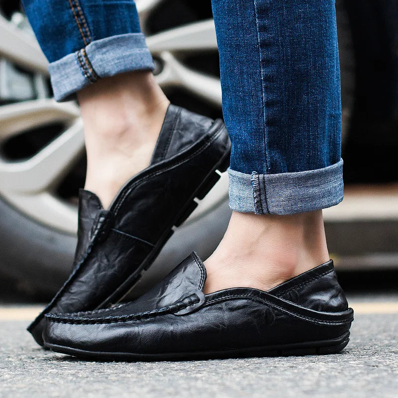 Chaussures mocassins en cuir noir pour homme, portées avec un jean bleu retroussé, devant une roue de voiture. Mode masculine élégante et décontractée.