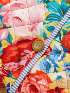 Gros plan d'une couverture matelassée à motifs floraux colorés avec boutons en bois et bordure rayée bleue et blanche. Design vibrant et décoratif.