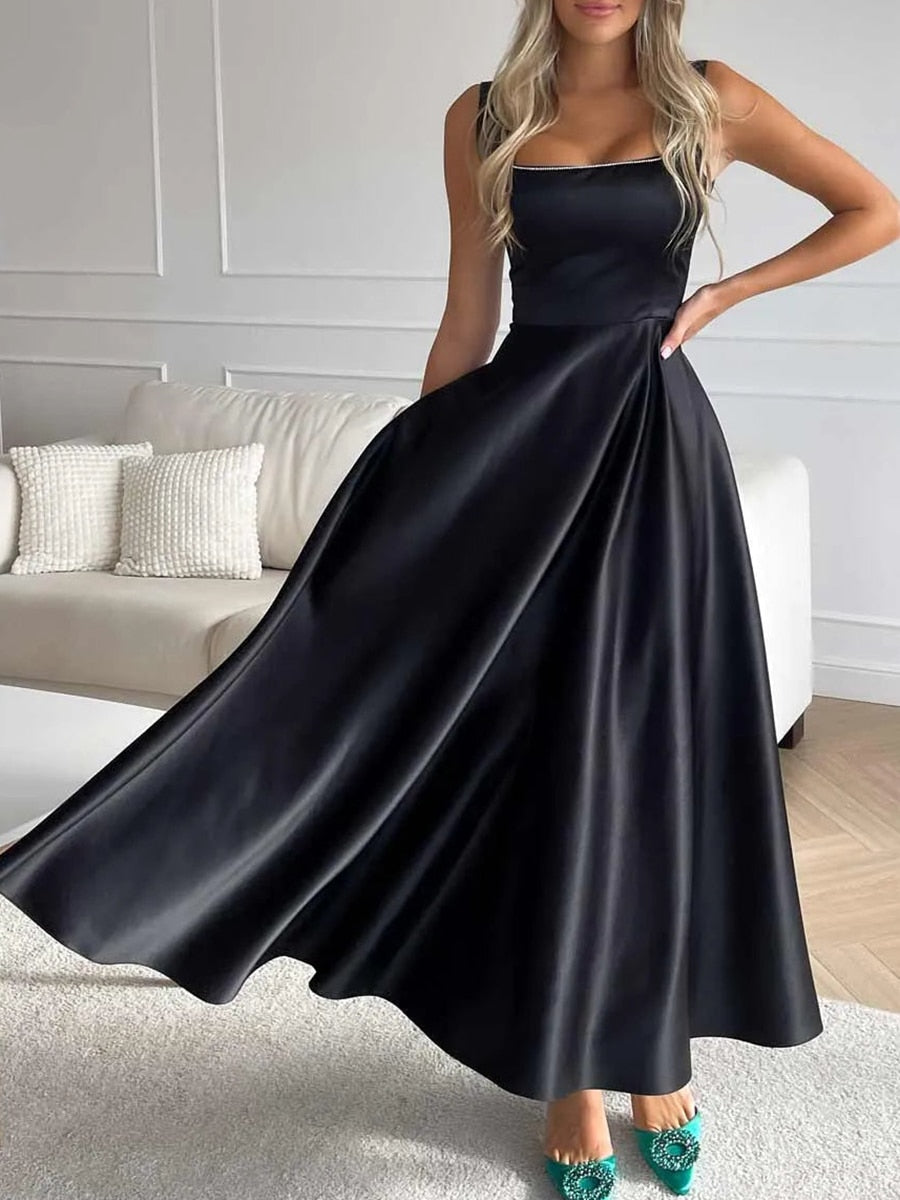 Robe longue noire élégante en satin, femme posant dans un salon moderne, chaussures vertes ornées, mode chic, tenue de soirée glamour.