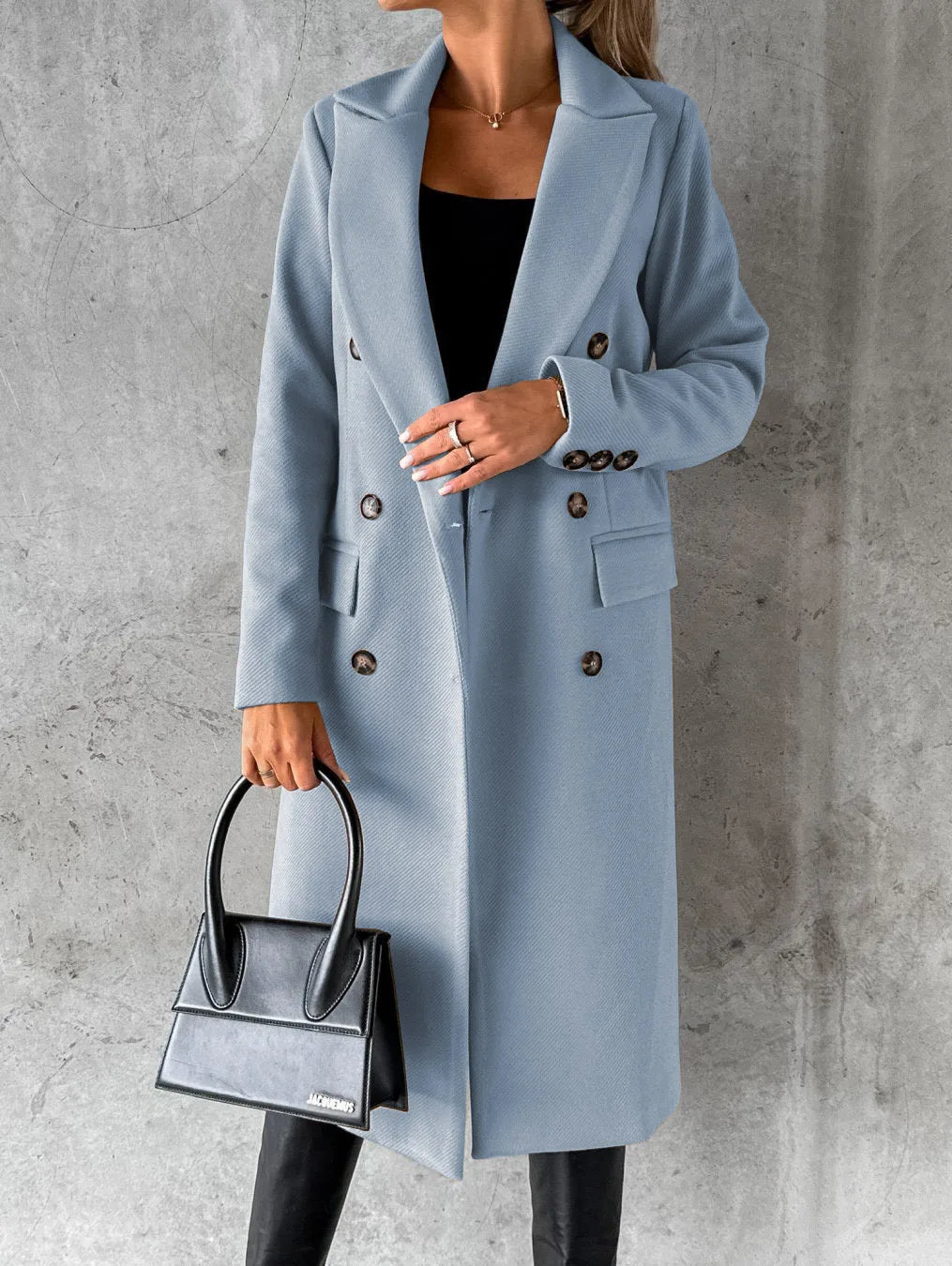 Femme portant un manteau bleu élégant, sac à main noir, fond gris. Mode automne, style chic, tenue sophistiquée, tendance vestimentaire.