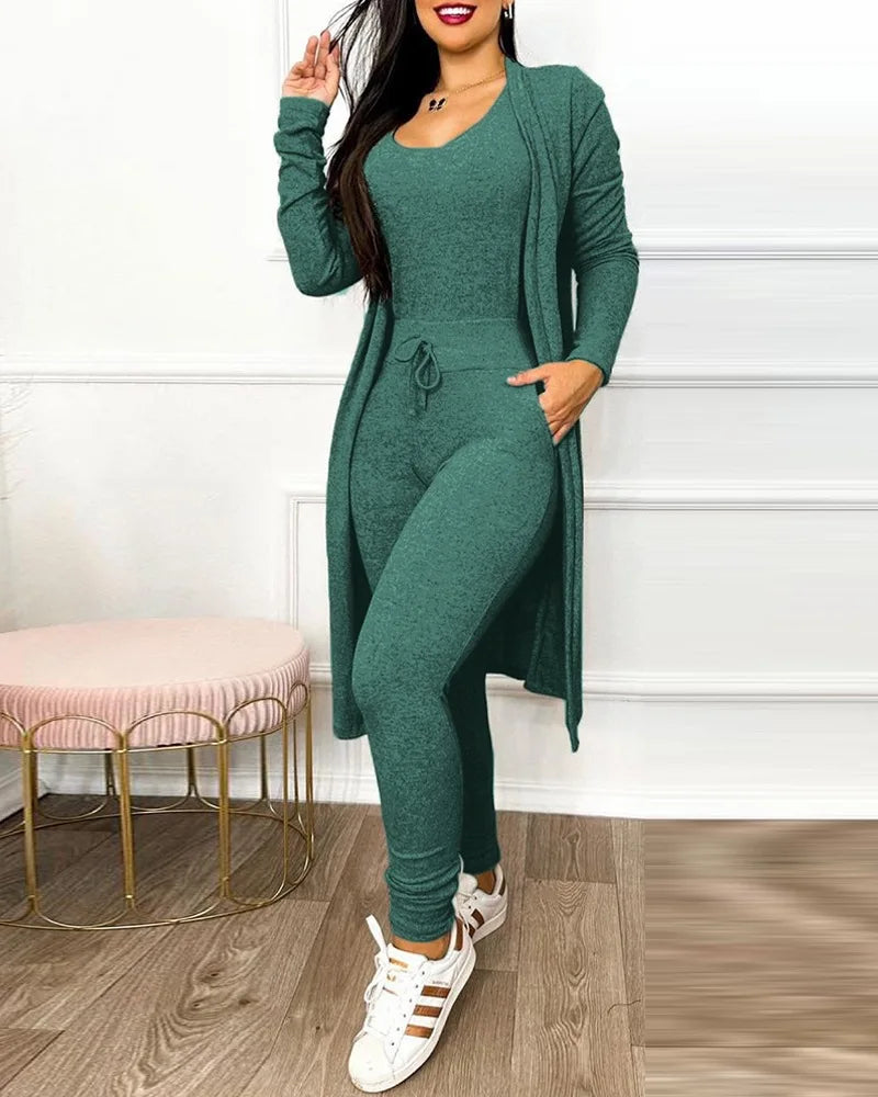 Femme portant un ensemble vert élégant, composé d'un cardigan long, d'un haut ajusté et d'un pantalon, avec des baskets blanches. Mode décontractée chic.