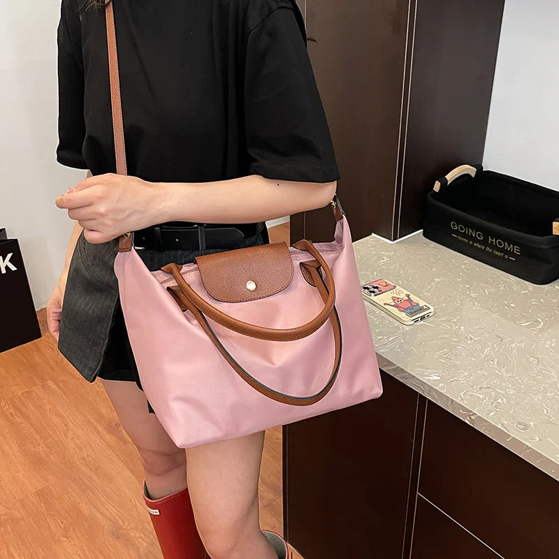 Sac à main rose en toile porté par une femme, avec des poignées en cuir marron, posé sur un comptoir moderne. Mode féminine, accessoire tendance.