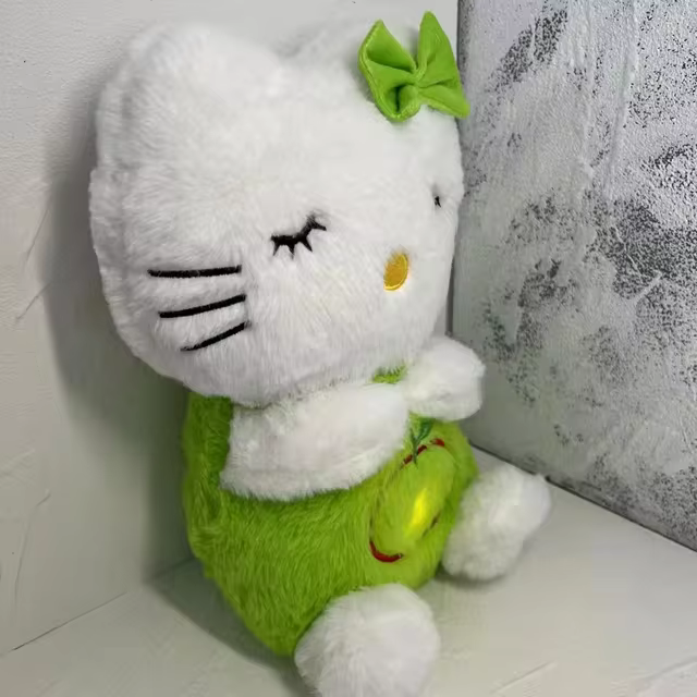 Peluche Hello Kitty blanche et verte avec nœud vert, assise contre un mur texturé. Jouet mignon, décoration chambre enfant, cadeau populaire.