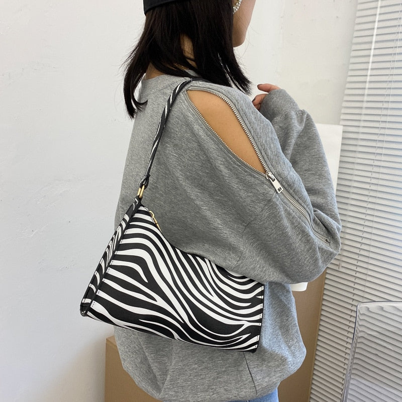 Sac à main zébré noir et blanc porté par une femme en pull gris à manches ouvertes, style moderne et tendance, accessoire mode chic.