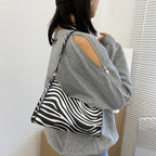 Sac à main zébré noir et blanc porté par une femme en pull gris à manches ouvertes, style moderne et tendance, accessoire mode chic.
