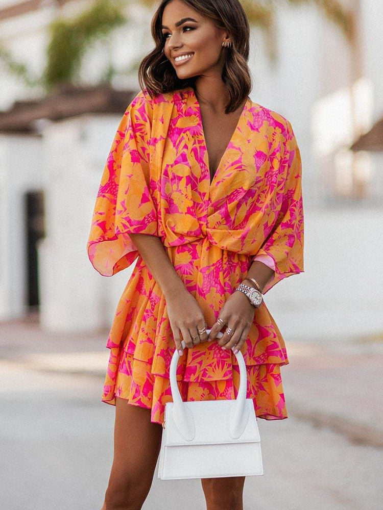Femme souriante portant une robe d'été orange et rose à motifs floraux, tenant un sac à main blanc. Mode estivale, tenue élégante et colorée.