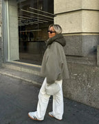 Femme en manteau oversize kaki, pantalon blanc, baskets Adidas, sac blanc, marchant en ville devant une vitrine. Mode urbaine décontractée.