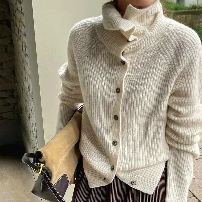 Femme portant un cardigan en laine beige avec col roulé, tenant un sac à main en cuir marron. Mode automne-hiver, style élégant et confortable.