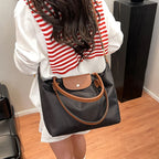 Femme portant un sac à main noir avec poignées marron, chemise blanche et pull rayé rouge. Mode élégante, accessoires tendance, style décontracté.