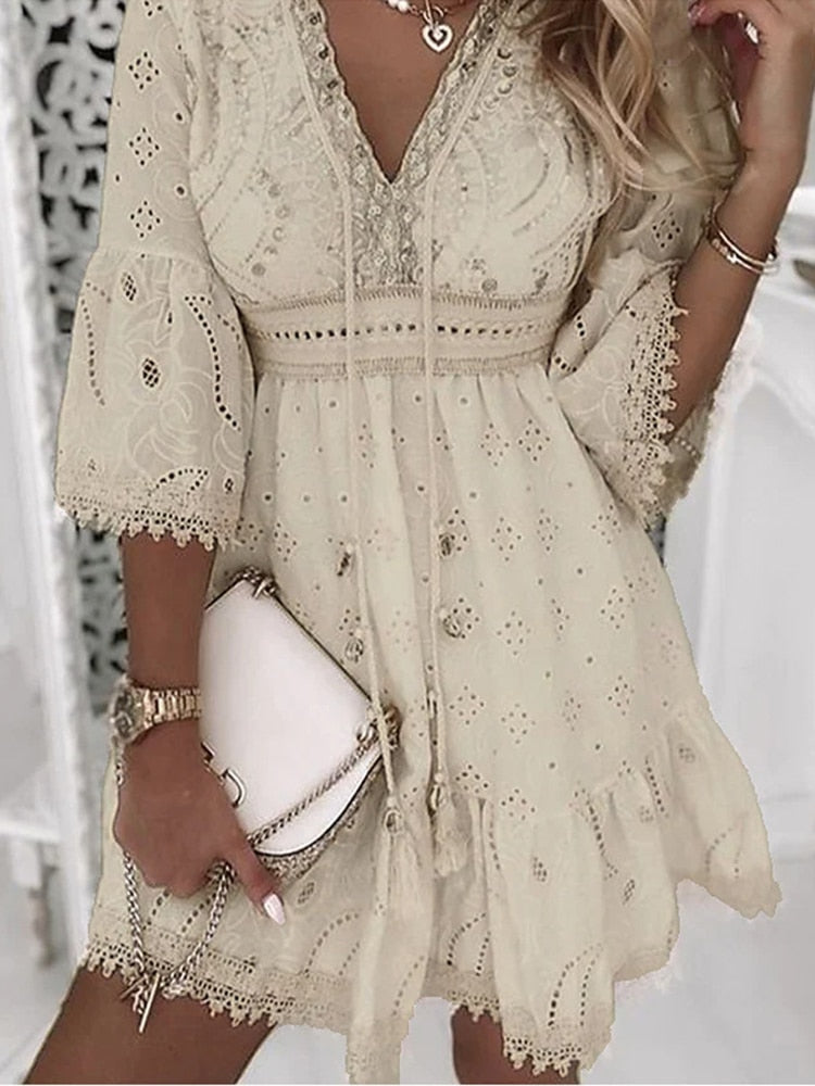 Robe bohème chic en dentelle beige avec manches évasées, détails brodés et col en V, accessoirisée d'un sac à main blanc élégant.