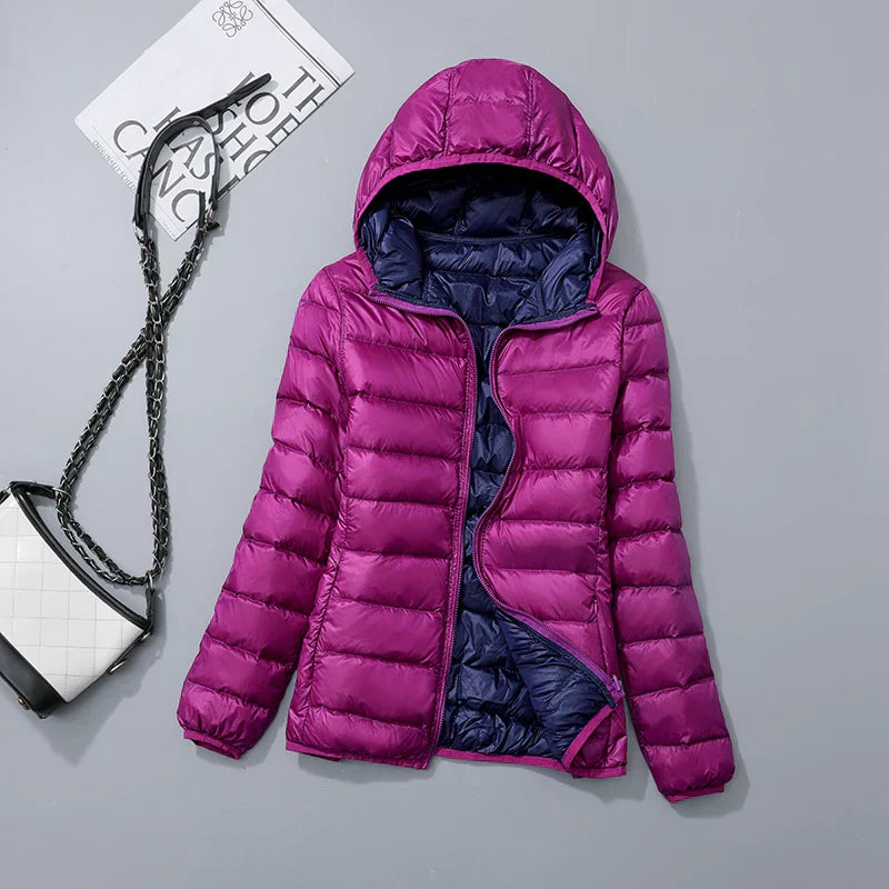 Doudoune violette à capuche pour femme, doublure bleue, posée à plat avec un sac à main blanc et noir en arrière-plan. Mode hiver tendance.