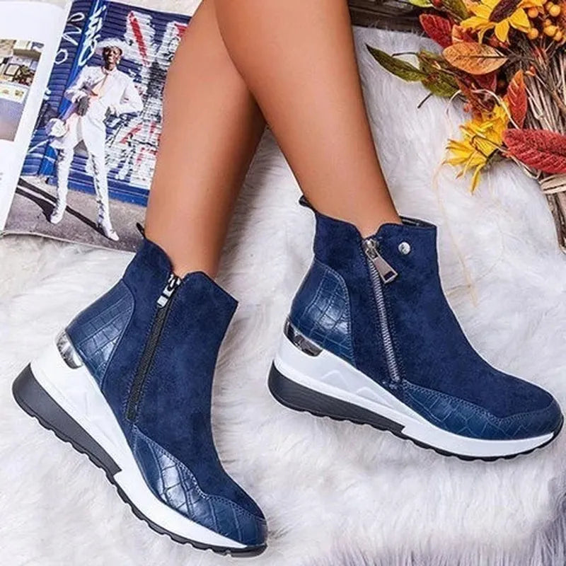 Bottes bleues en cuir avec fermeture éclair, semelle épaisse blanche et noire, posées sur un tapis blanc, à côté de feuilles d'automne et d'un magazine.