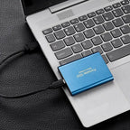 Disque SSD portable bleu connecté à un ordinateur portable argenté sur une surface en cuir noir. Stockage externe rapide et compact pour PC.