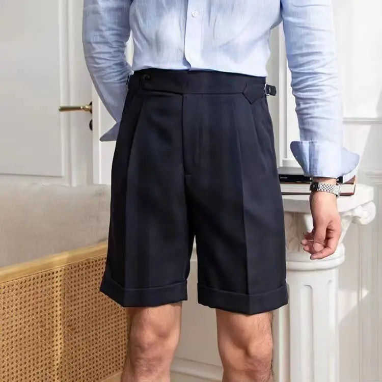 Homme portant un short habillé noir et une chemise bleue, debout dans un intérieur élégant. Mode masculine, tenue chic, style contemporain.