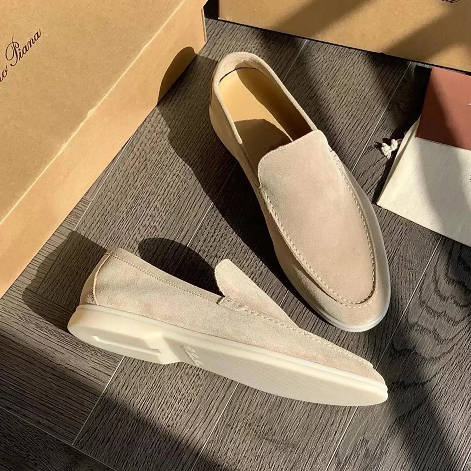 Mocassins en daim beige pour homme sur parquet en bois, éclairés par le soleil, avec boîte en carton. Chaussures élégantes et confortables.