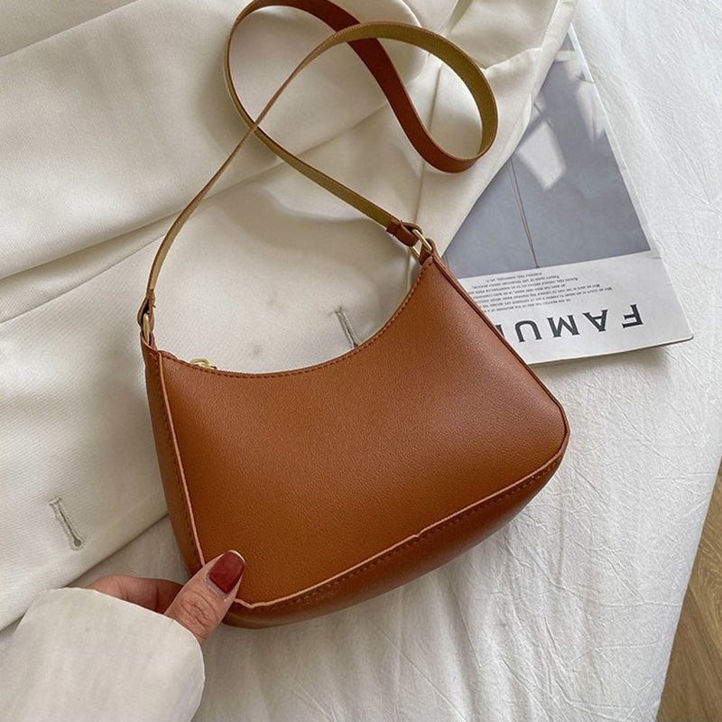 Sac à main en cuir marron sur un drap blanc, avec une bandoulière ajustable. Accessoire de mode élégant pour femme, tendance et chic.