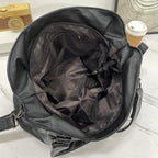 Sac à main en cuir noir ouvert sur une table en marbre, montrant l'intérieur vide. À côté, un gobelet de café en carton. Accessoire mode élégant.